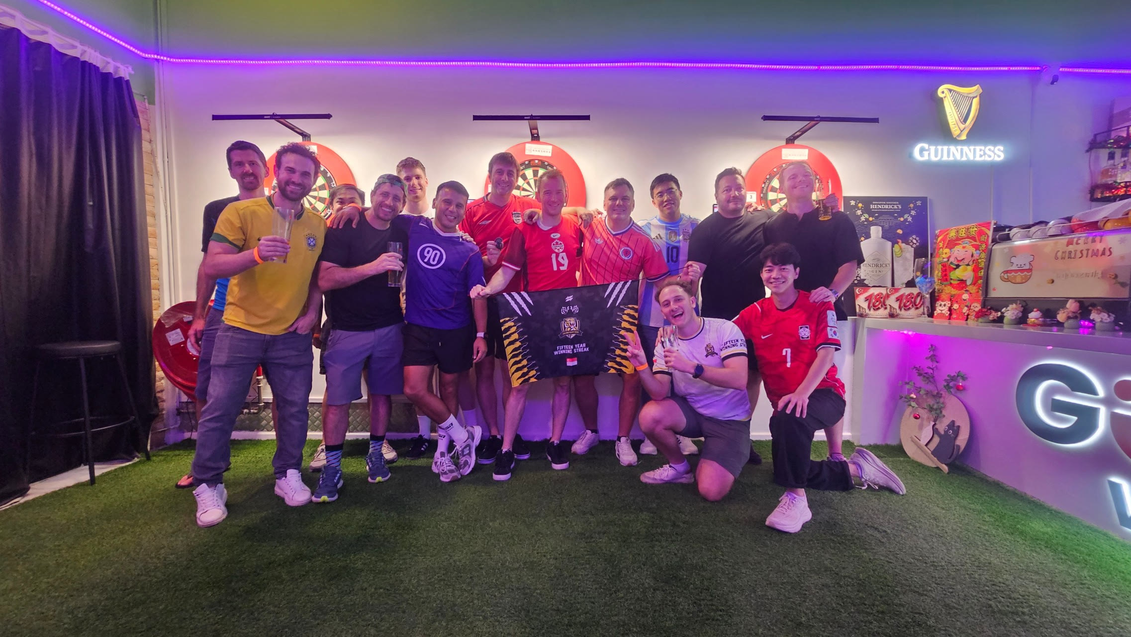 Football fans in team shirts posing together in front of the dartboards at Good Vibes Social Club